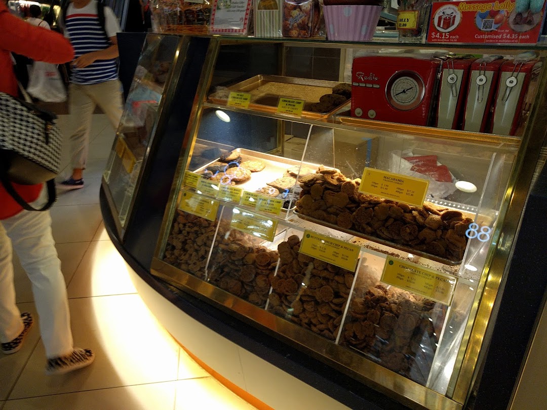 A glass display case at Famous Amos filled with various freshly baked cookies and merchandise.