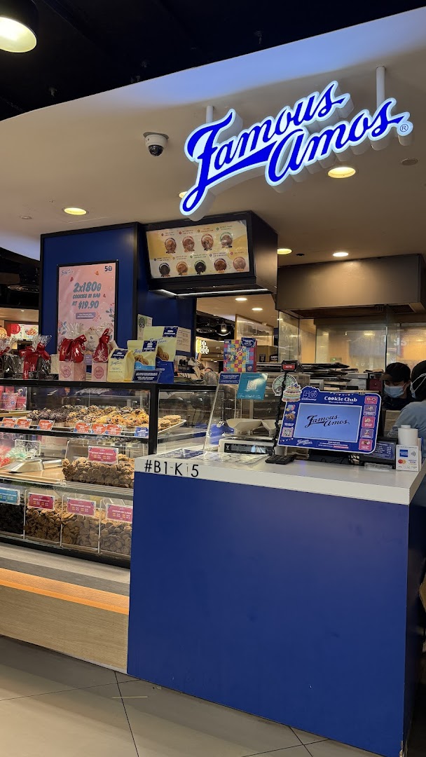 A vibrant Famous Amos cookie shop interior with display cases, counter, and prominent signage.