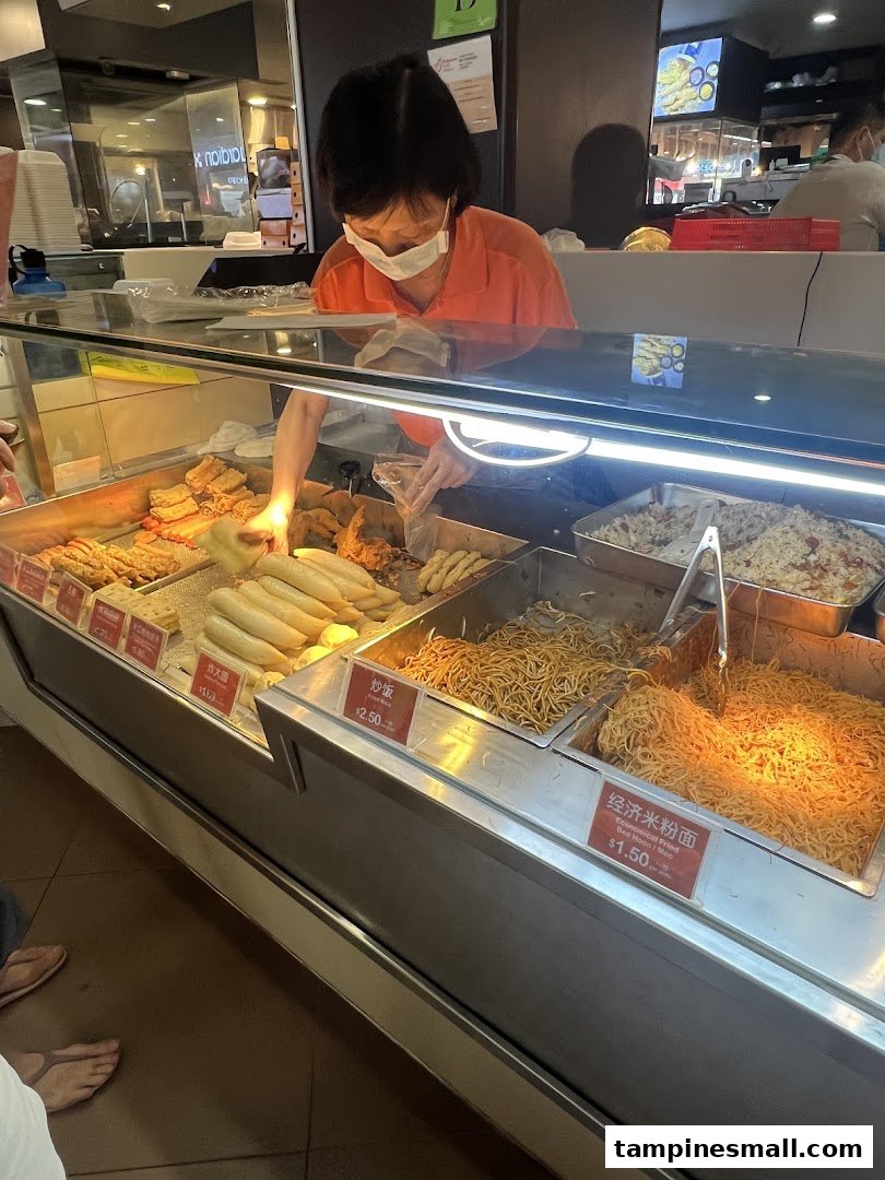 A staff member serves various fried items and noodles from a food display counter at Fei Siong.