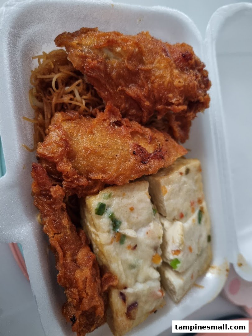 A close-up of fried chicken, tofu, and noodles in a takeaway box from Fei Siong.
