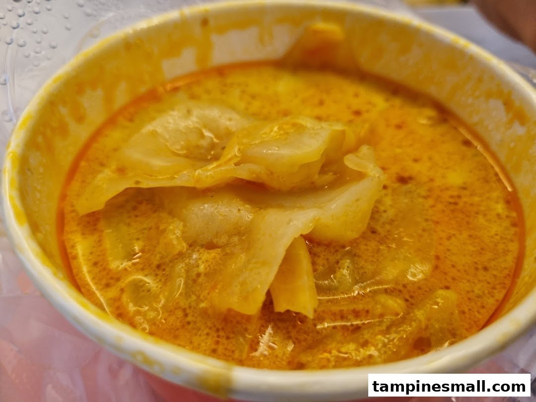 A close-up of a vibrant yellow curry dish with flat noodles or dumplings in a white bowl.