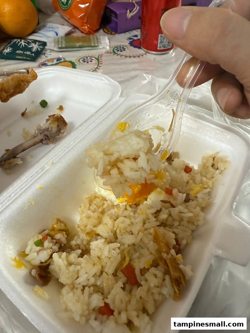 A close-up of delicious fried rice with egg and vegetables in a takeaway container.
