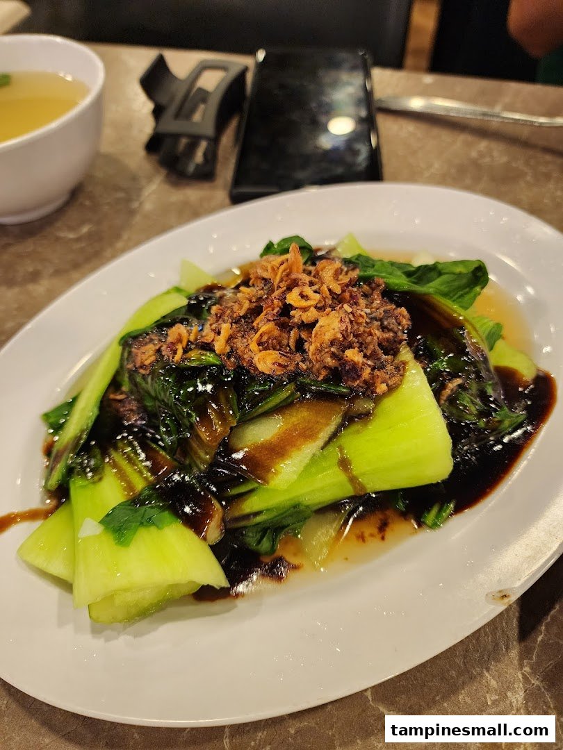 A plate of vibrant green bok choy with savory sauce and crispy fried toppings, served with soup.