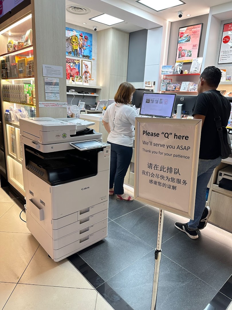 Customers and staff at FotoHub, featuring a large Canon printer and a queue sign for service.