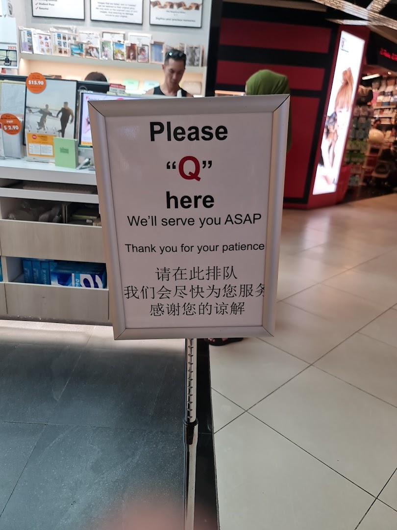 An interior shot of FotoHub showing a 'Please Q here' sign and a service counter.