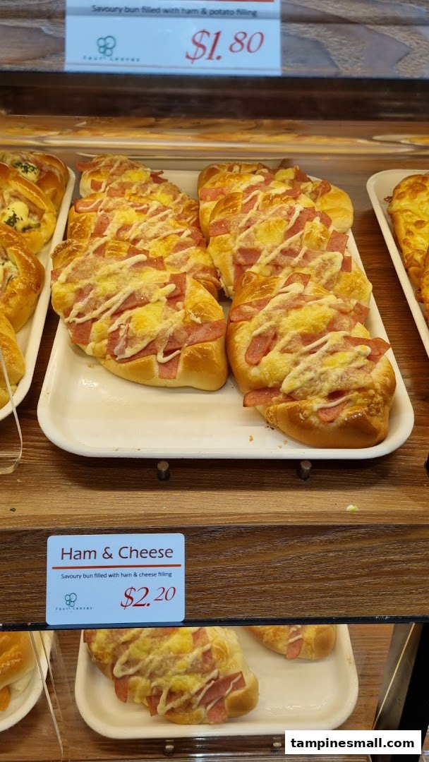 A display of freshly baked savoury buns with ham and cheese, and ham and potato fillings, with price tags.