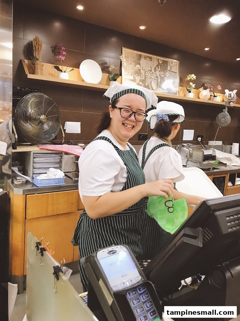 Two smiling staff members in uniform working behind the counter at Four Leaves bakery.