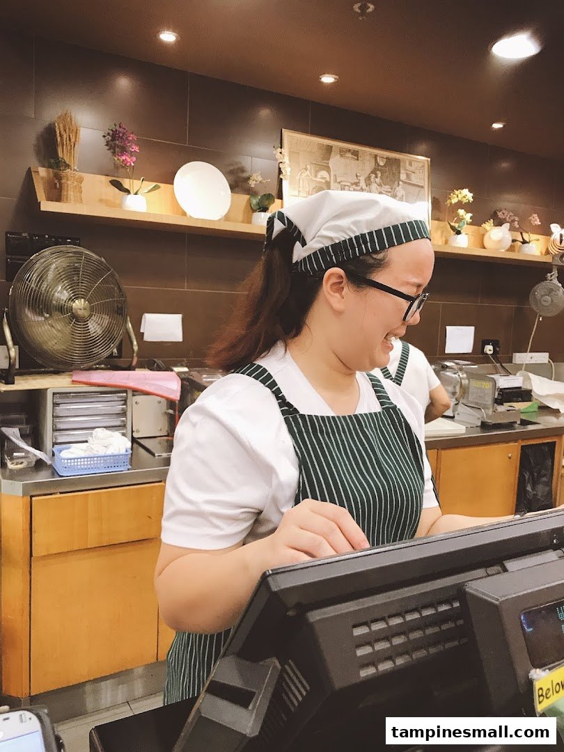A smiling staff member in a green apron works at the counter of Four Leaves bakery.