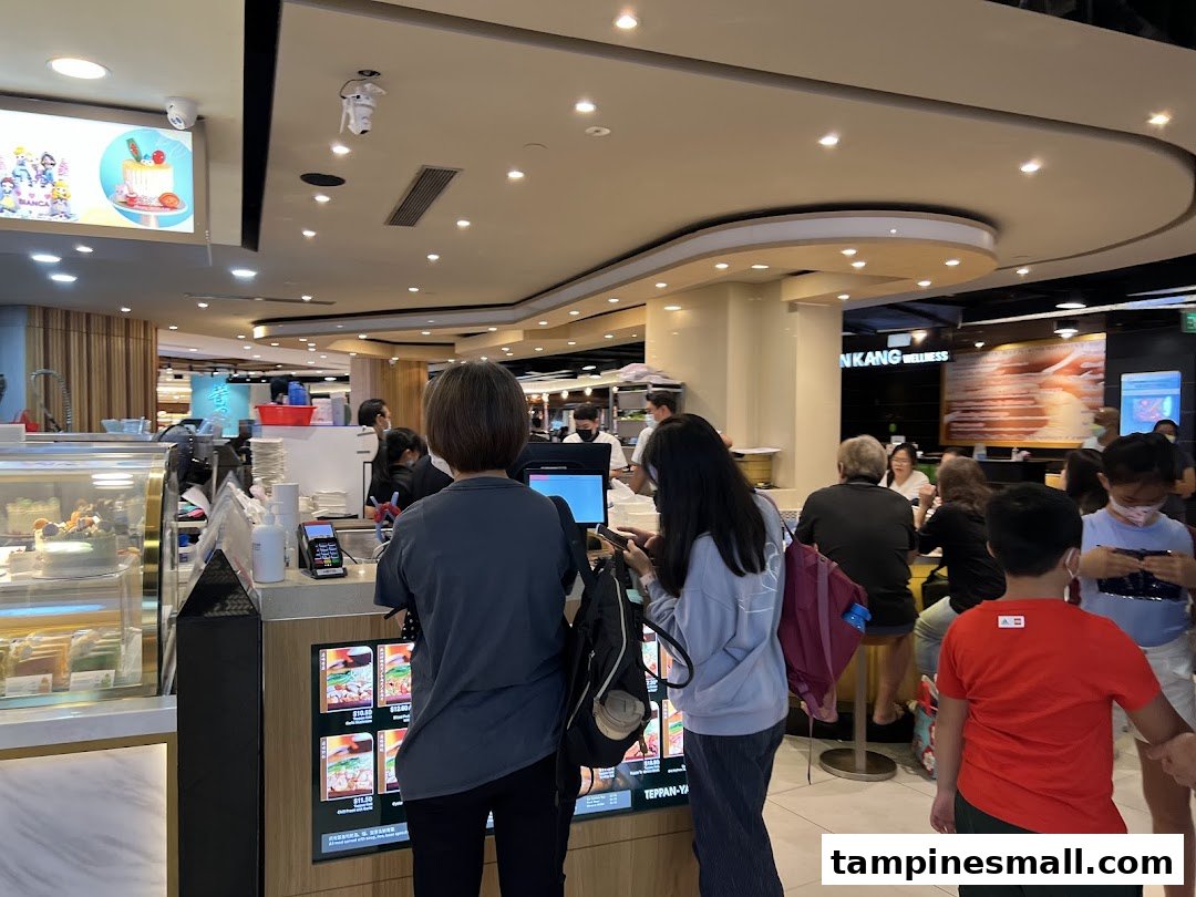 Customers at a bakery counter, with cakes in display cases and a busy interior.