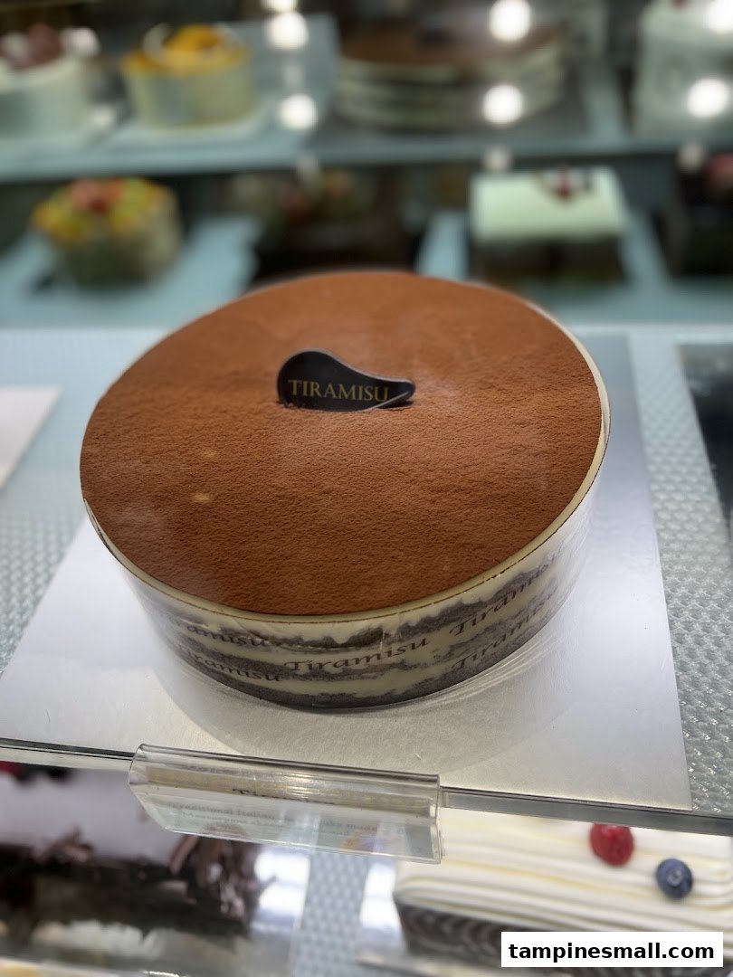 A large, decadent tiramisu cake displayed prominently in a bakery's refrigerated case.