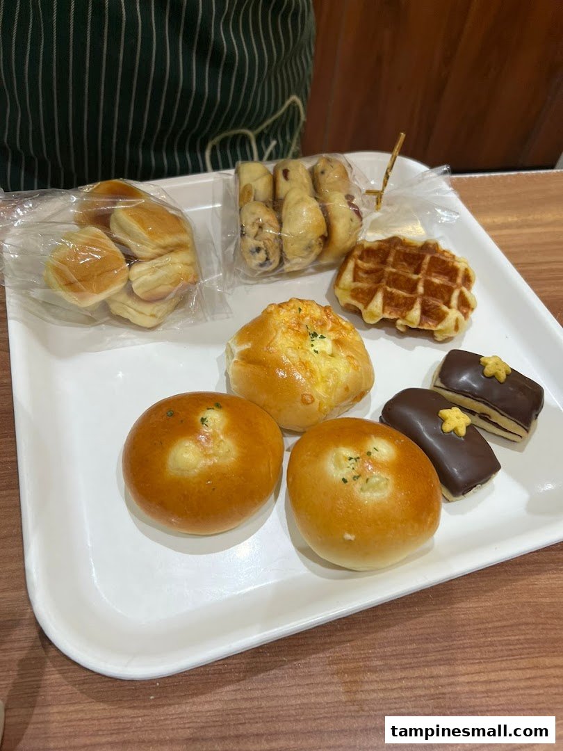 A white tray filled with various freshly baked pastries, including buns, waffles, and chocolate treats.