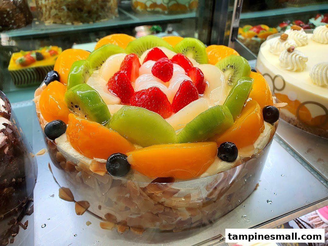 A vibrant fruit tart with kiwi, strawberries, peaches, and blueberries displayed in a bakery.