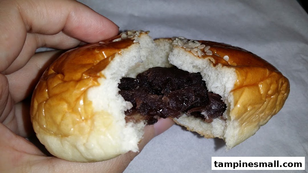 A hand holds a freshly baked bun, split open to reveal a rich red bean paste filling.
