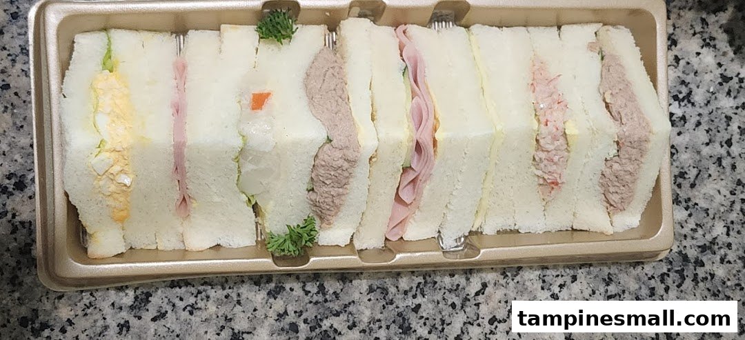 A tray of assorted fresh sandwiches with various fillings, including egg, ham, and tuna.