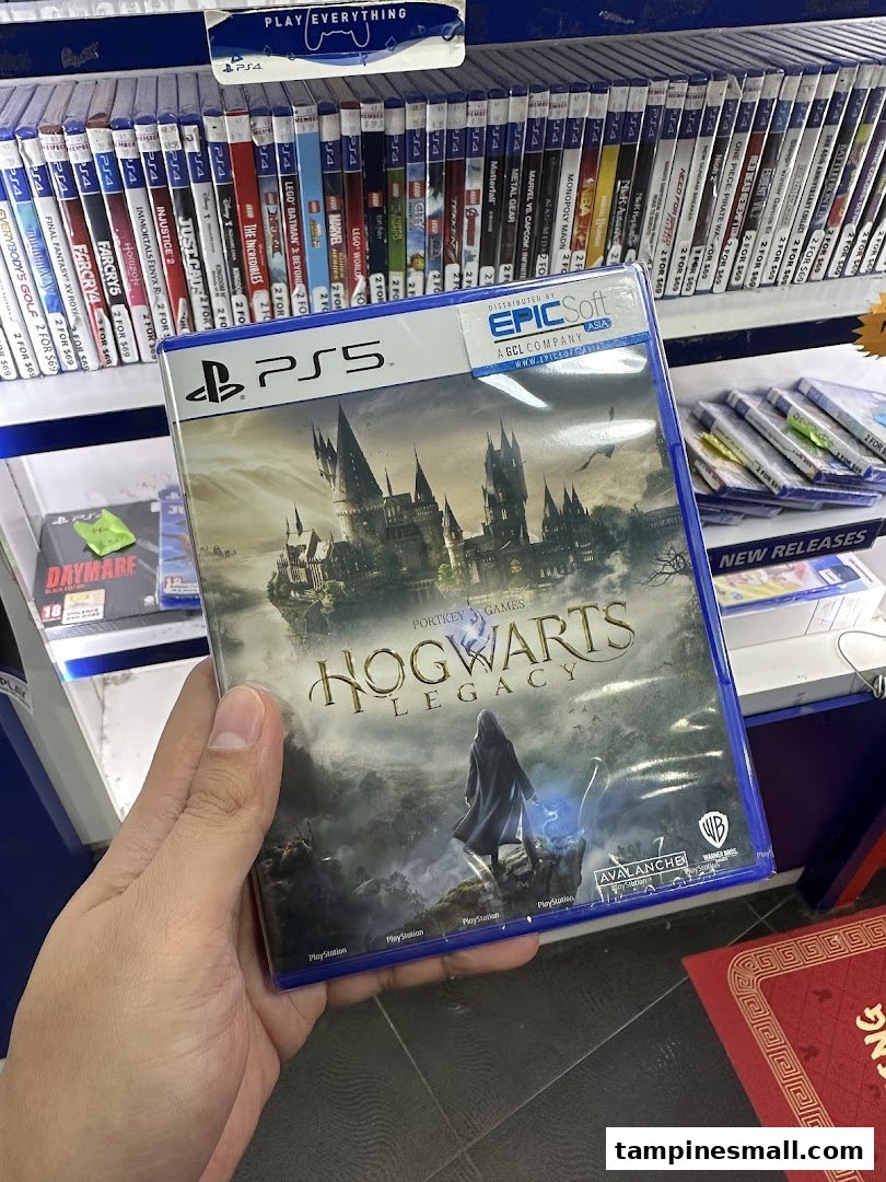 A hand holds a PS5 Hogwarts Legacy game case in a retail store, surrounded by other video games.
