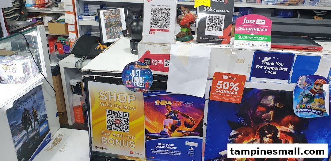 An interior view of GameXtreme Tampines, showcasing game posters, payment options, and merchandise at the counter.