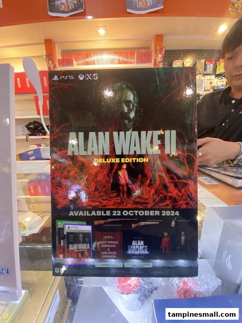 A large 'Alan Wake II Deluxe Edition' game poster displayed prominently inside GameXtreme Tampines, with a staff member visible.