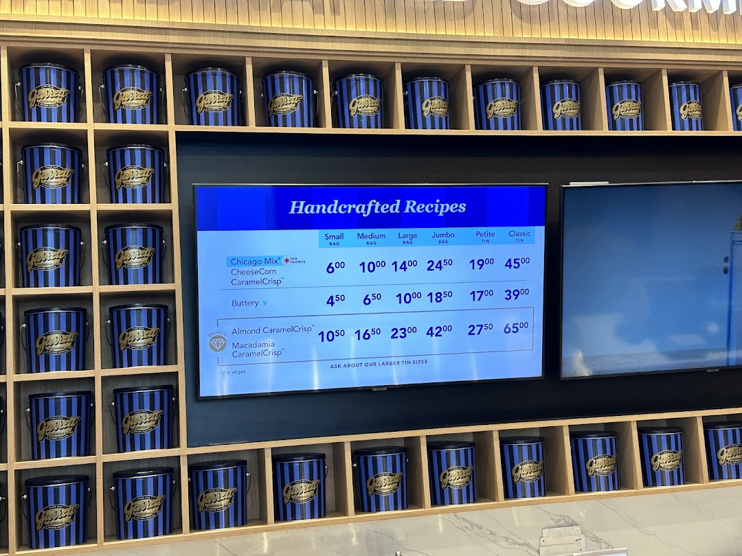 Digital menu board displaying Garrett Popcorn flavors and prices, surrounded by branded popcorn tins.
