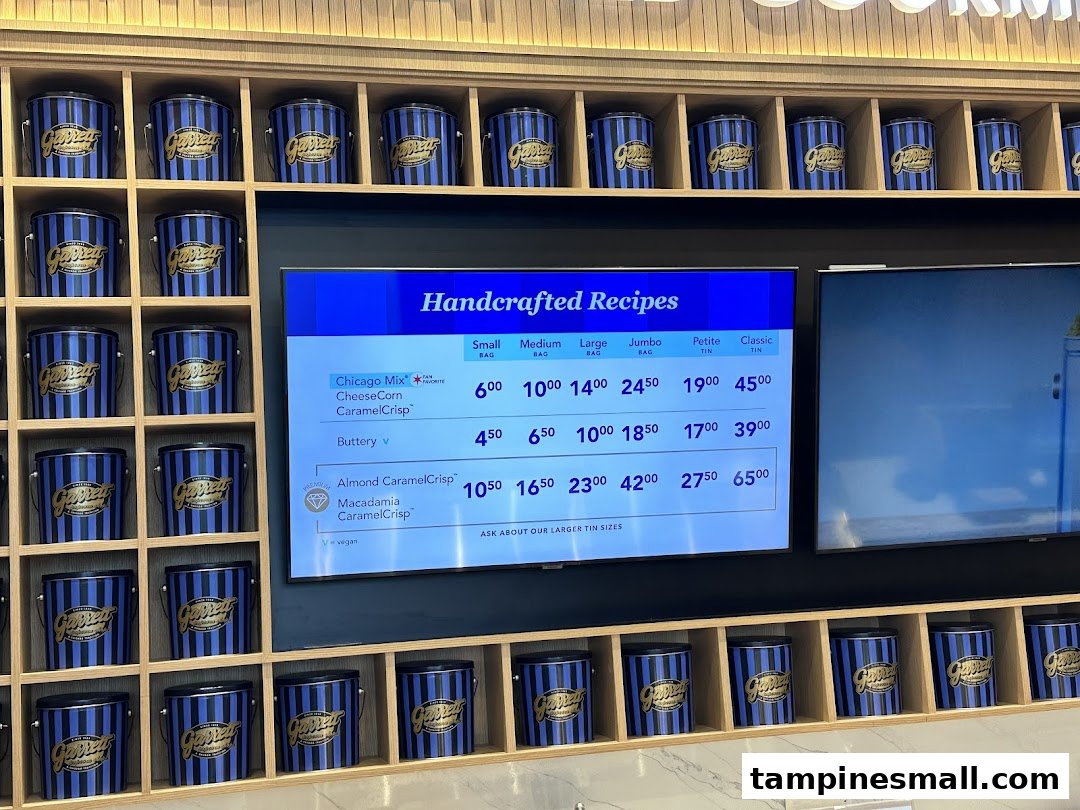 Digital menu board displaying Garrett Popcorn flavors and prices, surrounded by branded popcorn tins.