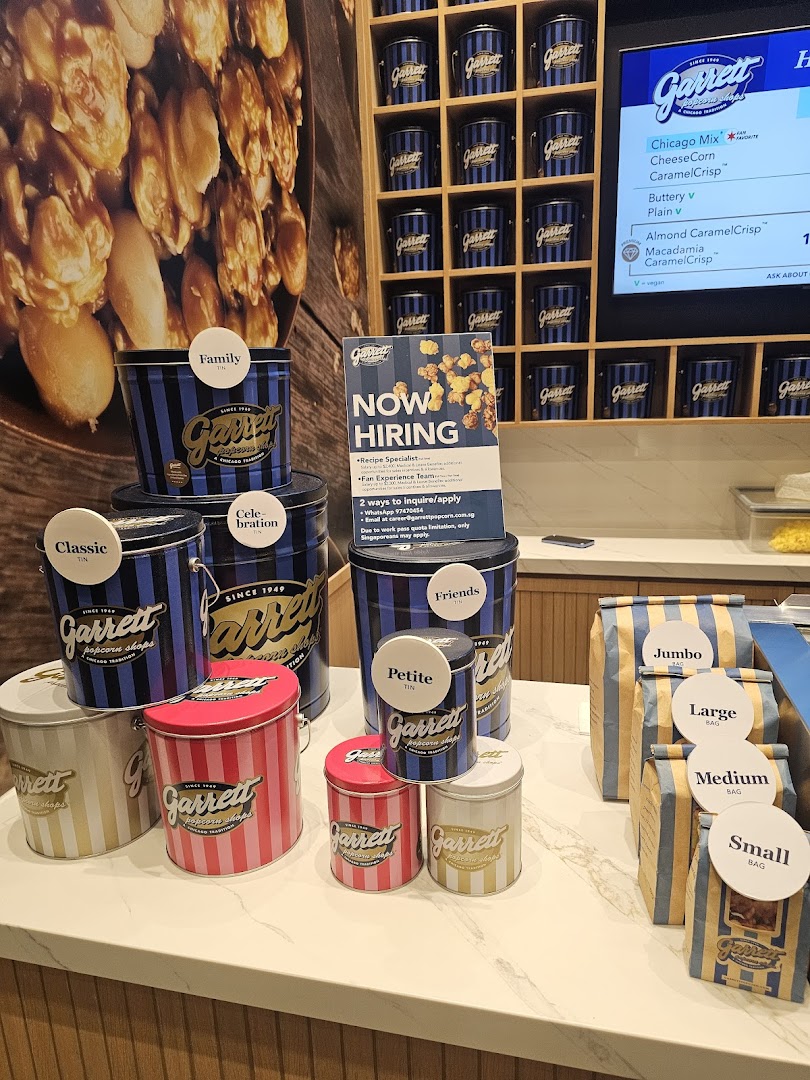 An interior view of Garrett Popcorn Shops, showcasing various popcorn tins, bags, and a digital menu.