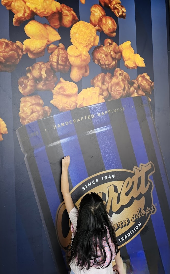 A child interacts with a large wall graphic featuring Garrett Popcorn and its iconic blue and black striped bucket.
