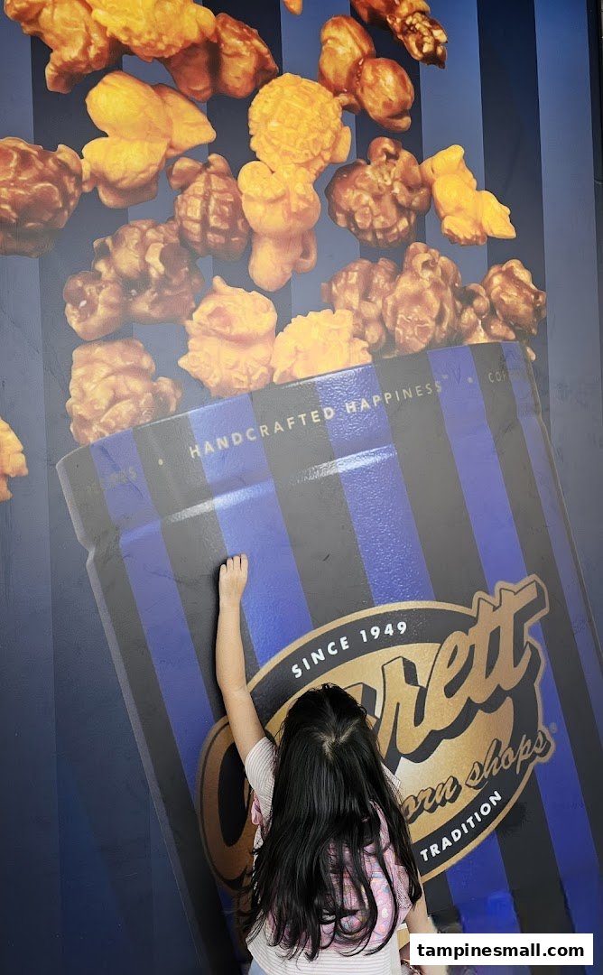 A child interacts with a large wall graphic featuring Garrett Popcorn and its iconic blue and black striped bucket.