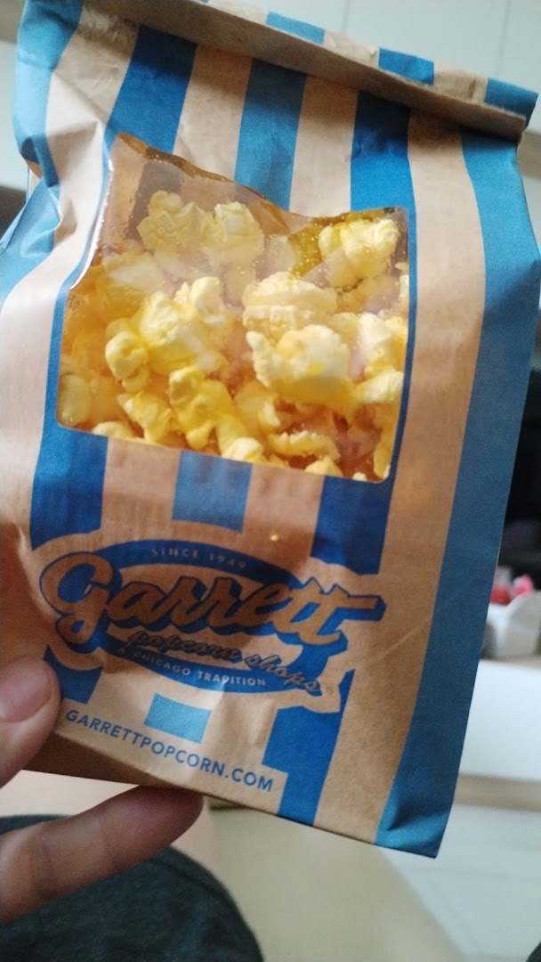 A hand holds a brown and blue striped bag of Garrett Popcorn, filled with yellow popcorn.