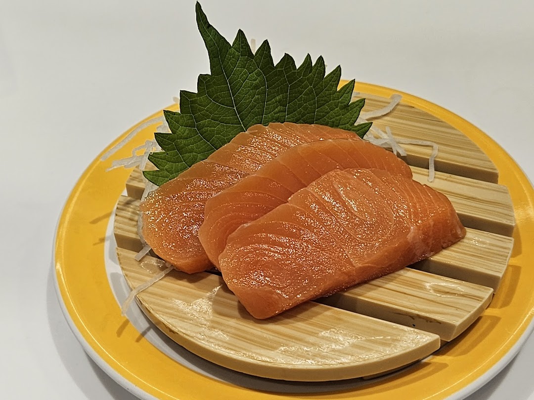 Close-up of fresh salmon sashimi slices served on a yellow plate with a green shiso leaf.