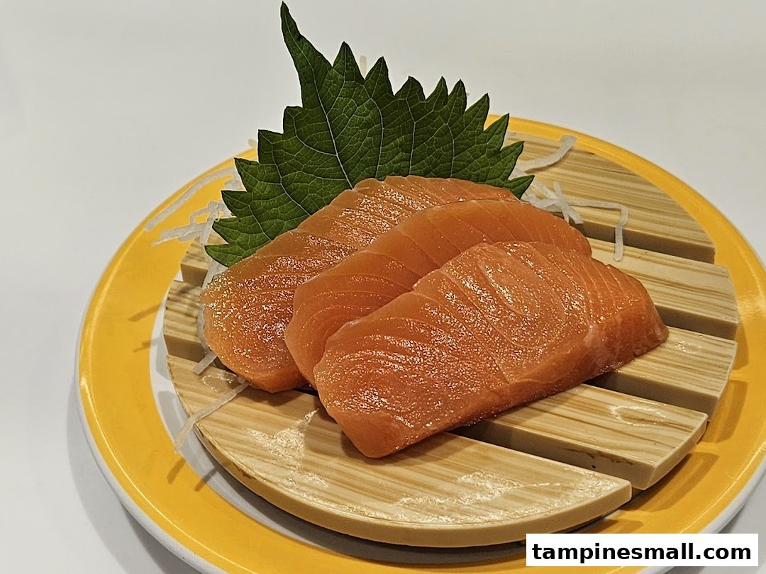 Close-up of fresh salmon sashimi slices served on a yellow plate with a green shiso leaf.