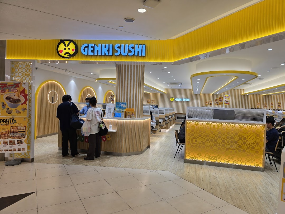 The vibrant yellow entrance of Genki Sushi at Tampines Mall, with customers at the counter.