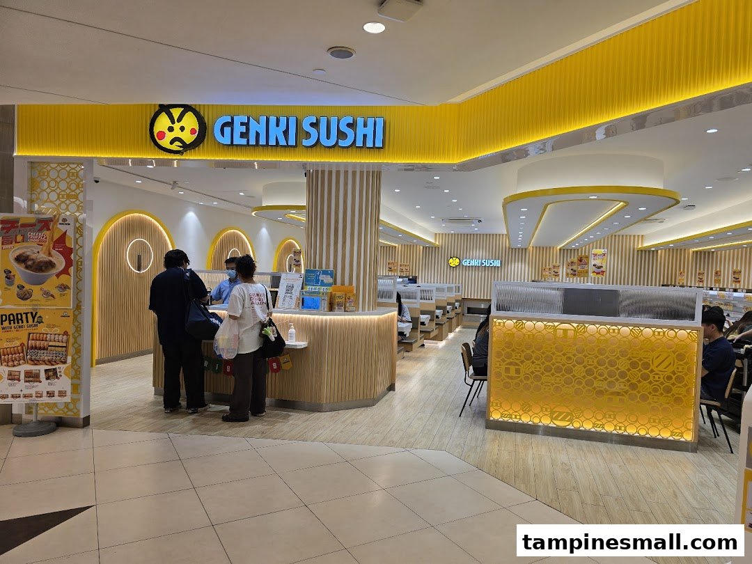 The vibrant yellow entrance of Genki Sushi at Tampines Mall, with customers at the counter.