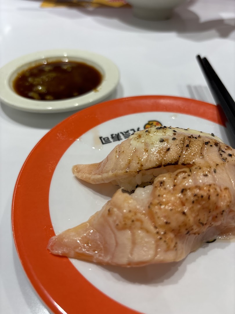 Close-up of two pieces of seared salmon sushi on a plate with a side of sauce.