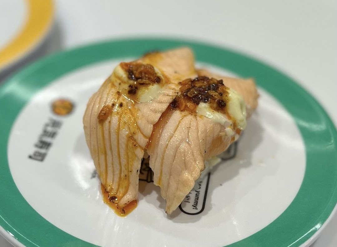 A close-up of two pieces of seared salmon sushi with sauce on a white and green plate.