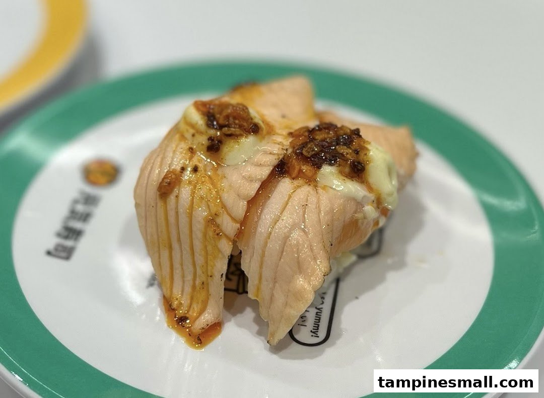 A close-up of two pieces of seared salmon sushi with sauce on a white and green plate.