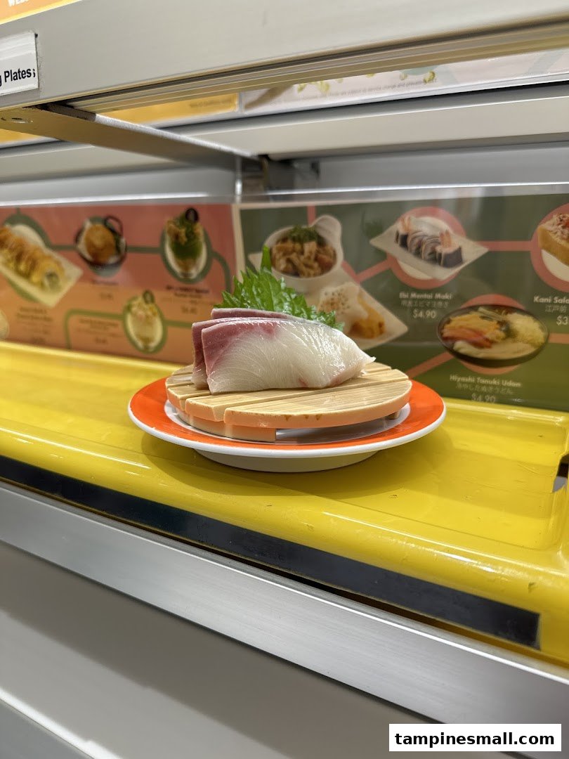 A fresh sushi dish on a conveyor belt with menu items and prices displayed in the background.