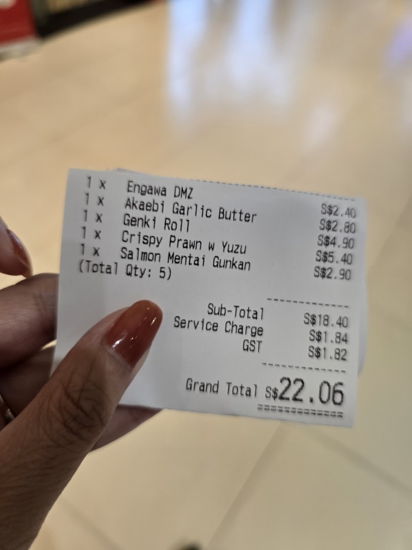 A hand holds a Genki Sushi receipt detailing five food items and the total cost of S$22.06.