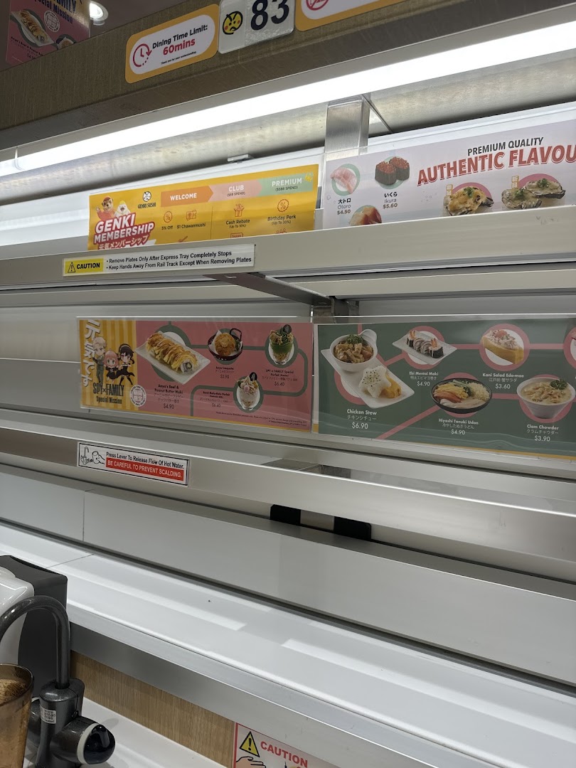 Interior view of Genki Sushi, showcasing various menu items, promotions, and the conveyor belt system.
