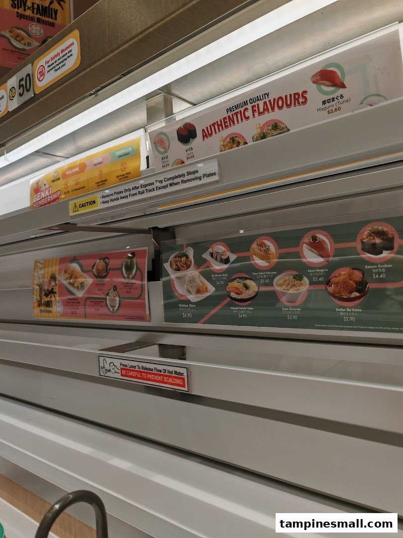 Close-up of a sushi conveyor belt displaying various fresh sushi and hot food items with prices.