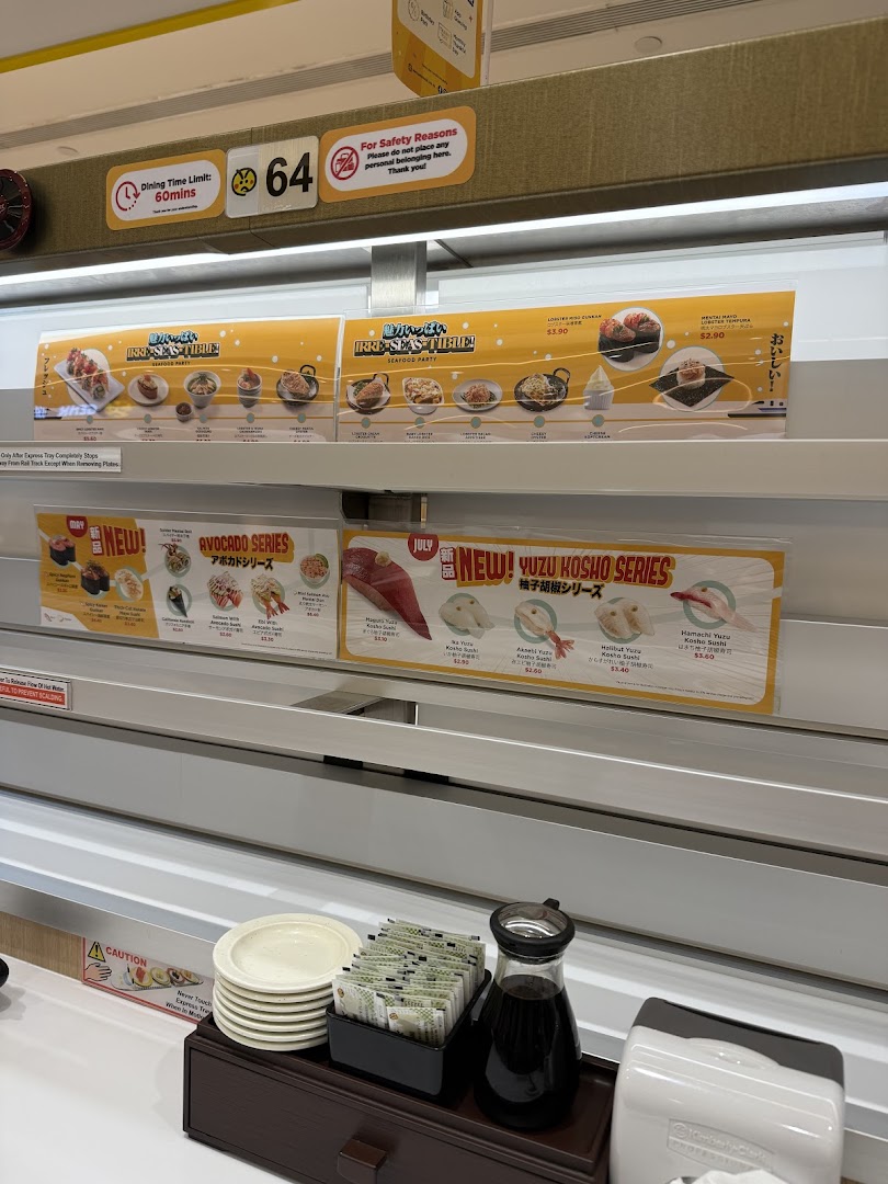 Interior view of Genki Sushi, featuring the conveyor belt system, promotional displays, and table condiments.