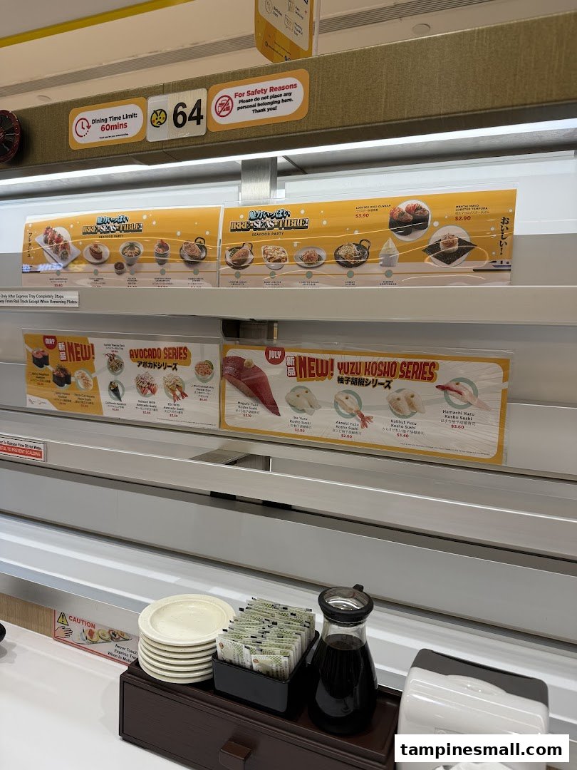 Interior view of Genki Sushi, featuring the conveyor belt system, promotional displays, and table condiments.