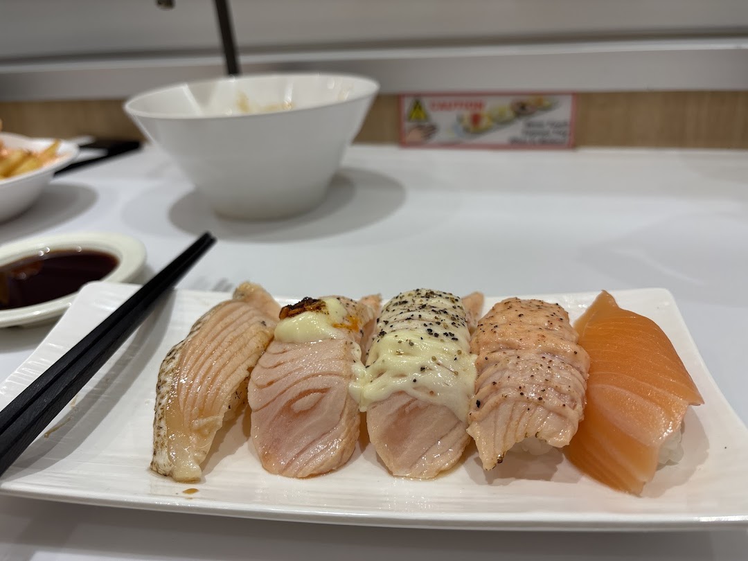 A plate of fresh salmon sushi, including seared and plain varieties, served with chopsticks and soy sauce.