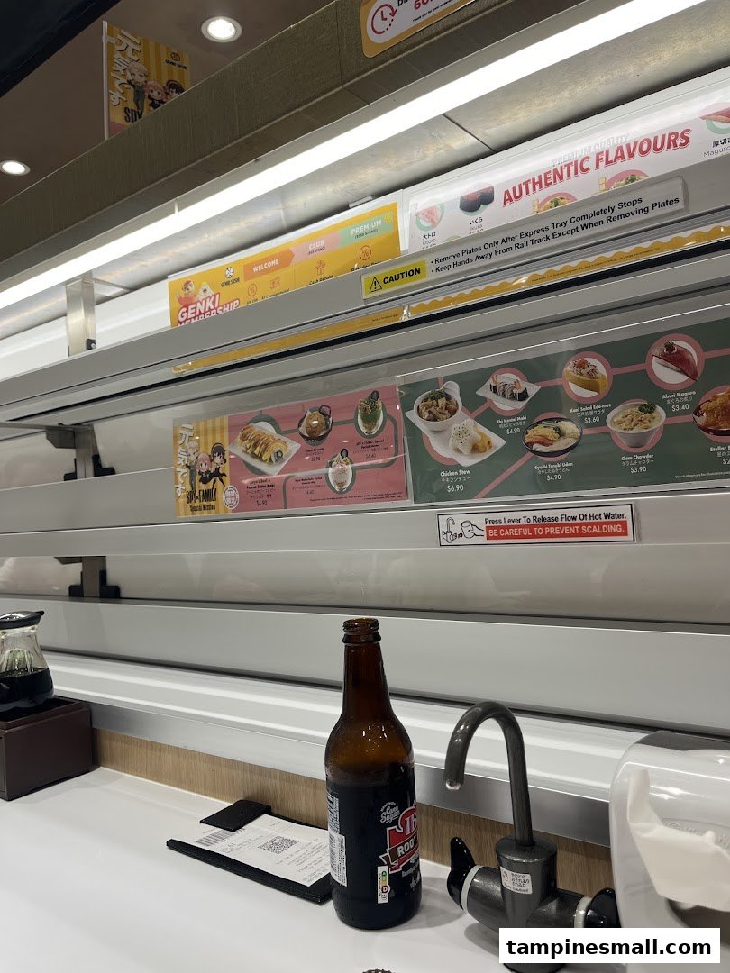 Interior view of Genki Sushi, showcasing the express conveyor belt system, a table setting, and food displays.