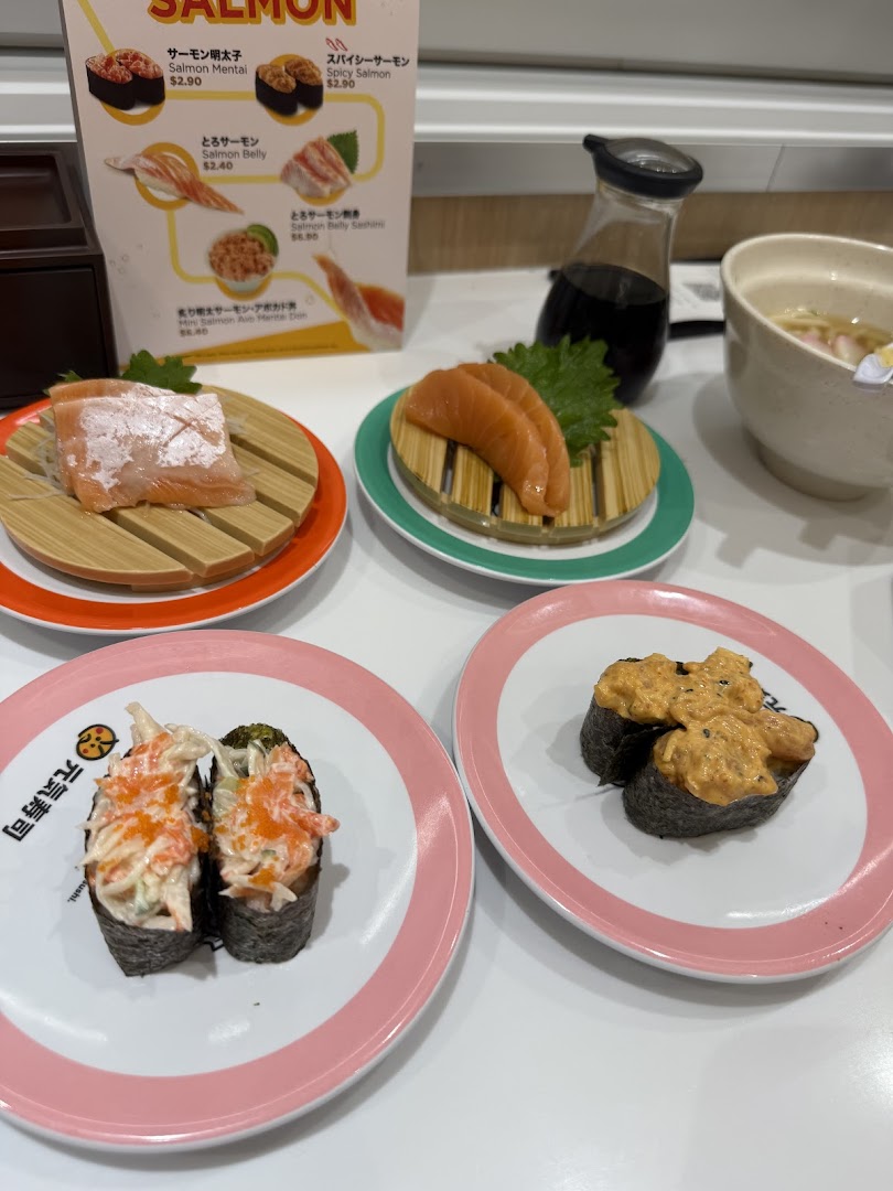A table view of various sushi dishes, including salmon and gunkan maki, with a menu board in the background.