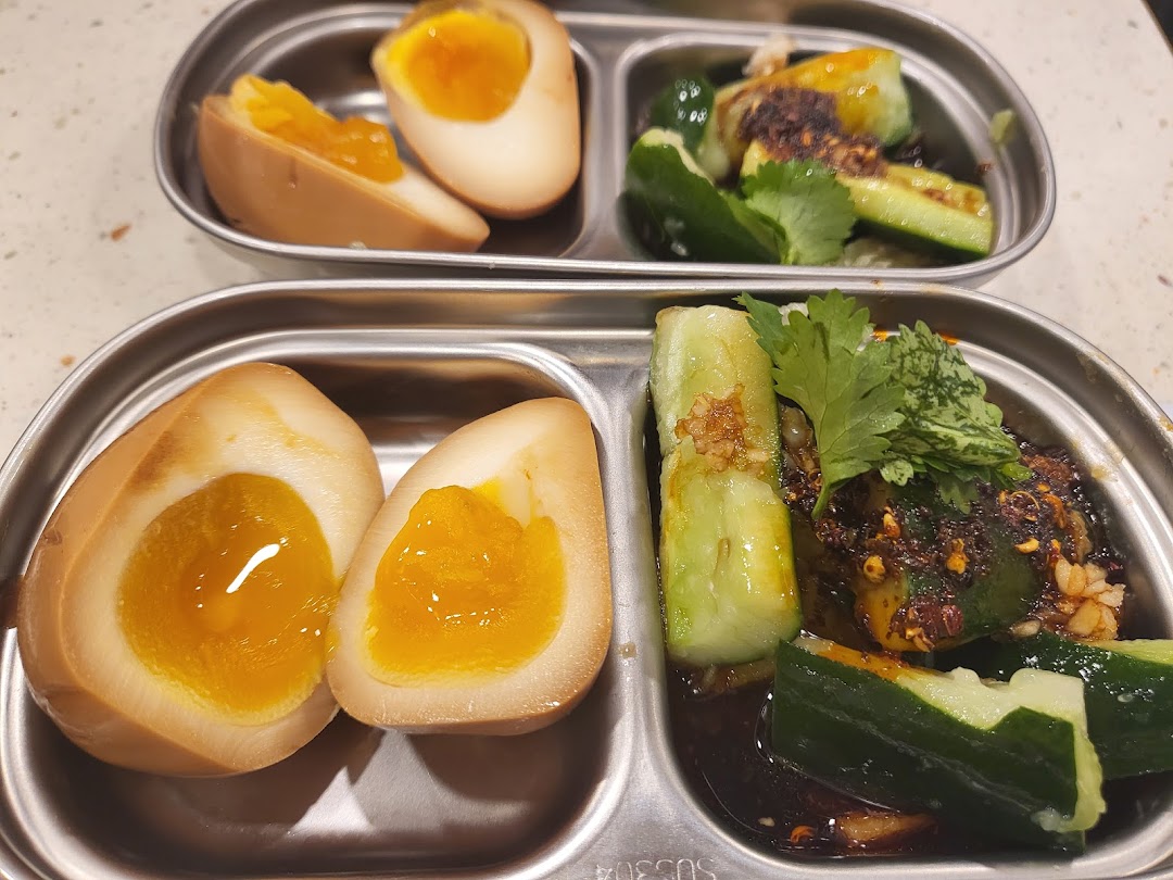Two metal trays featuring perfectly cooked tea eggs and spicy cucumber salad.