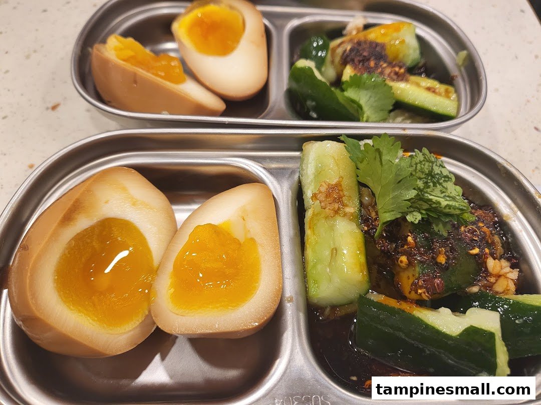 Two metal trays featuring perfectly cooked tea eggs and spicy cucumber salad.