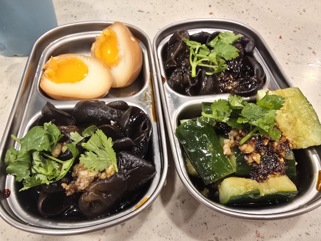 Assorted side dishes including tea eggs, wood ear mushrooms, and cucumbers served in metal trays.