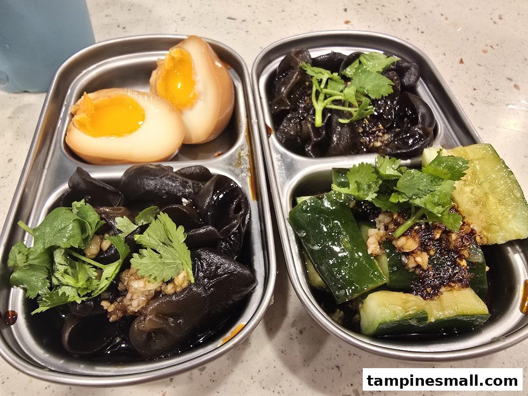 Assorted side dishes including tea eggs, wood ear mushrooms, and cucumbers served in metal trays.