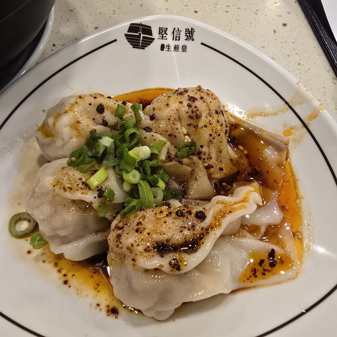 A plate of spicy wontons or dumplings garnished with green onions and chili oil.