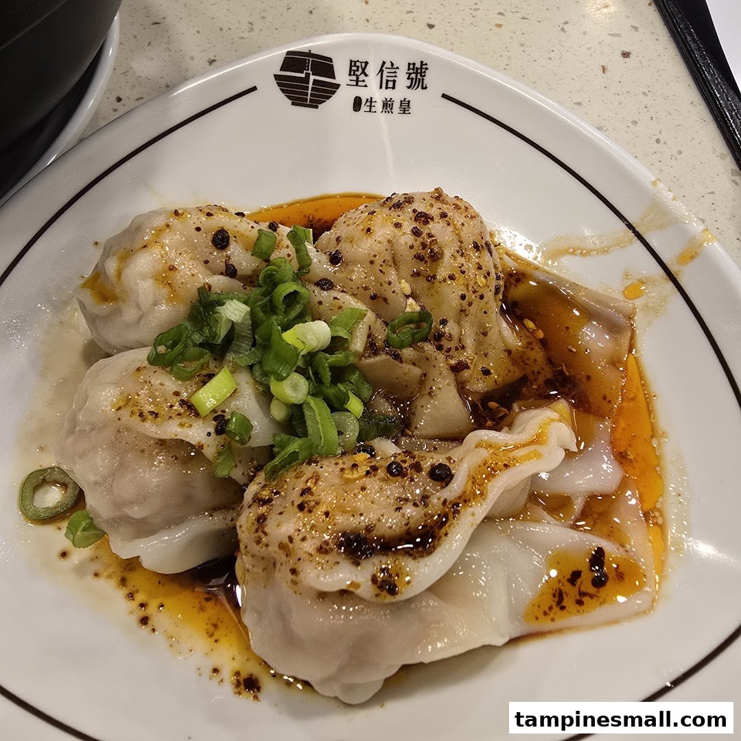 A plate of spicy wontons or dumplings garnished with green onions and chili oil.