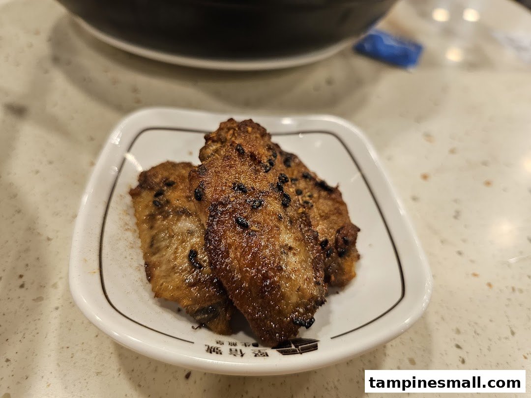 A plate of crispy, seasoned chicken wings with black sesame seeds on a white dish.